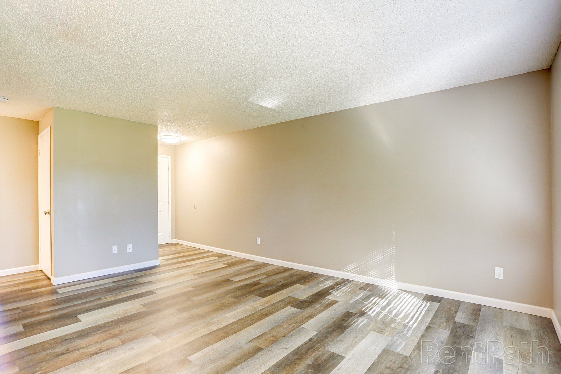 An empty living room with hardwood floors and beige walls.