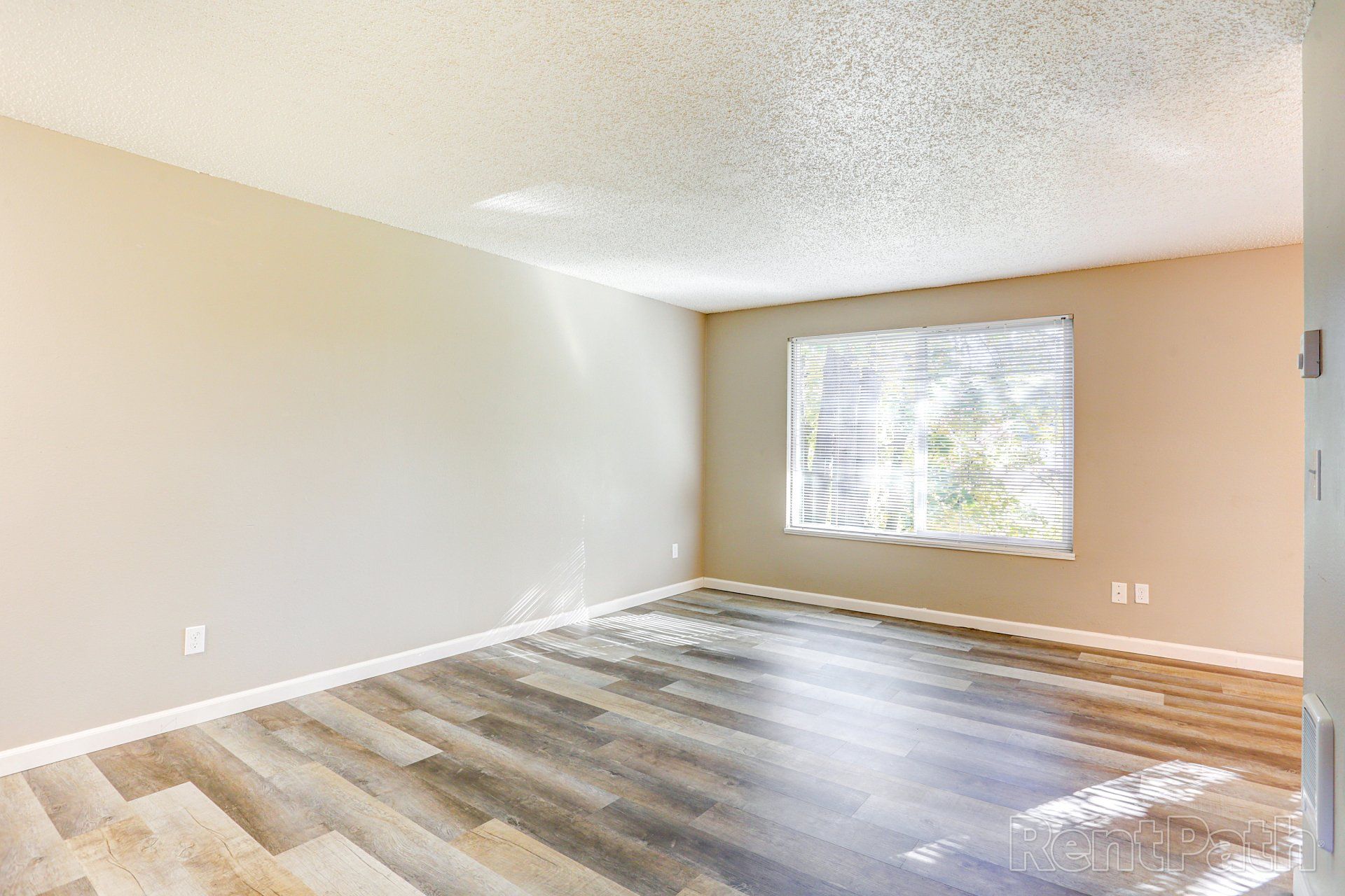 An empty living room with hardwood floors and a large window.