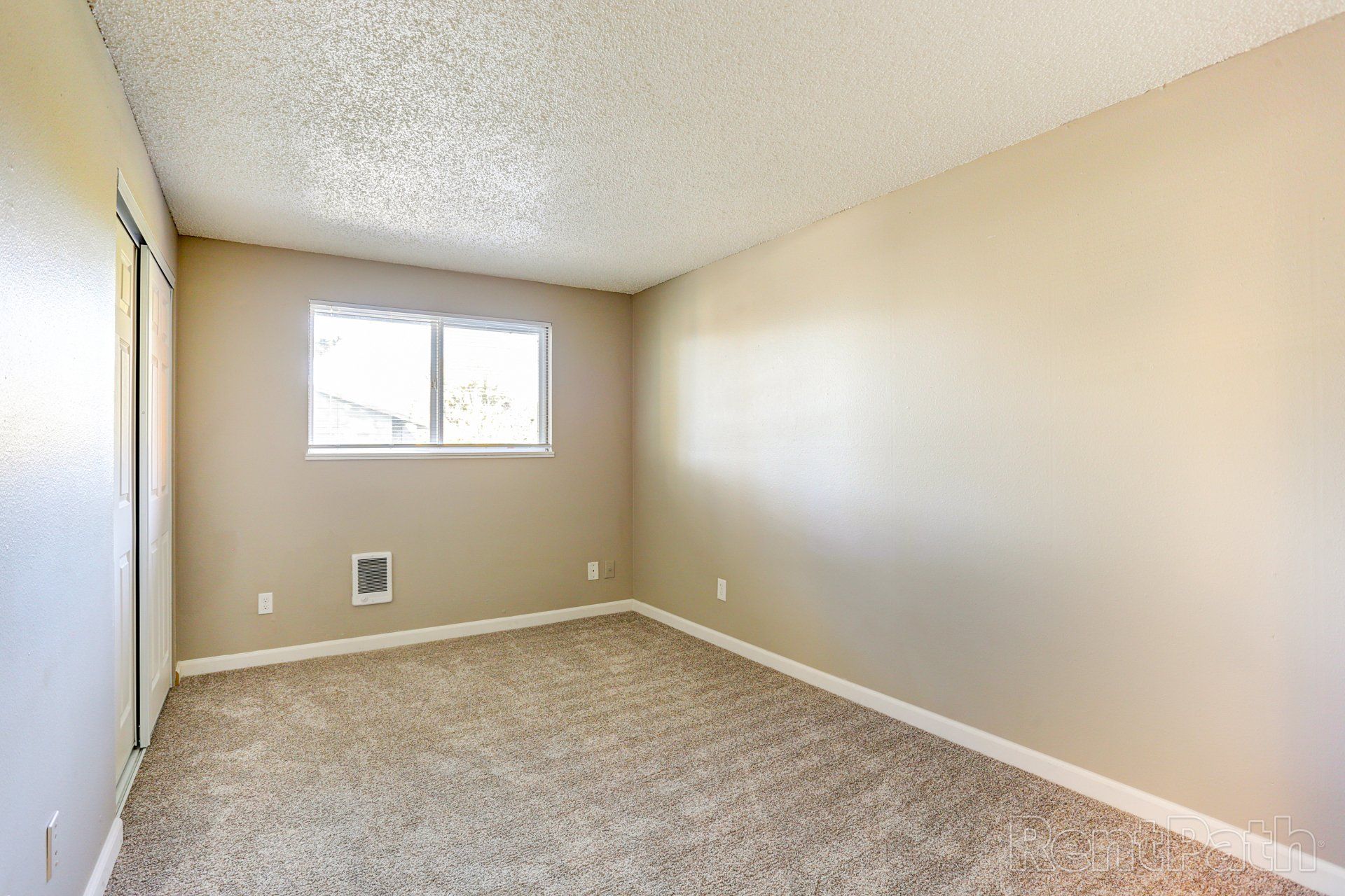 An empty bedroom with a window and a carpeted floor.