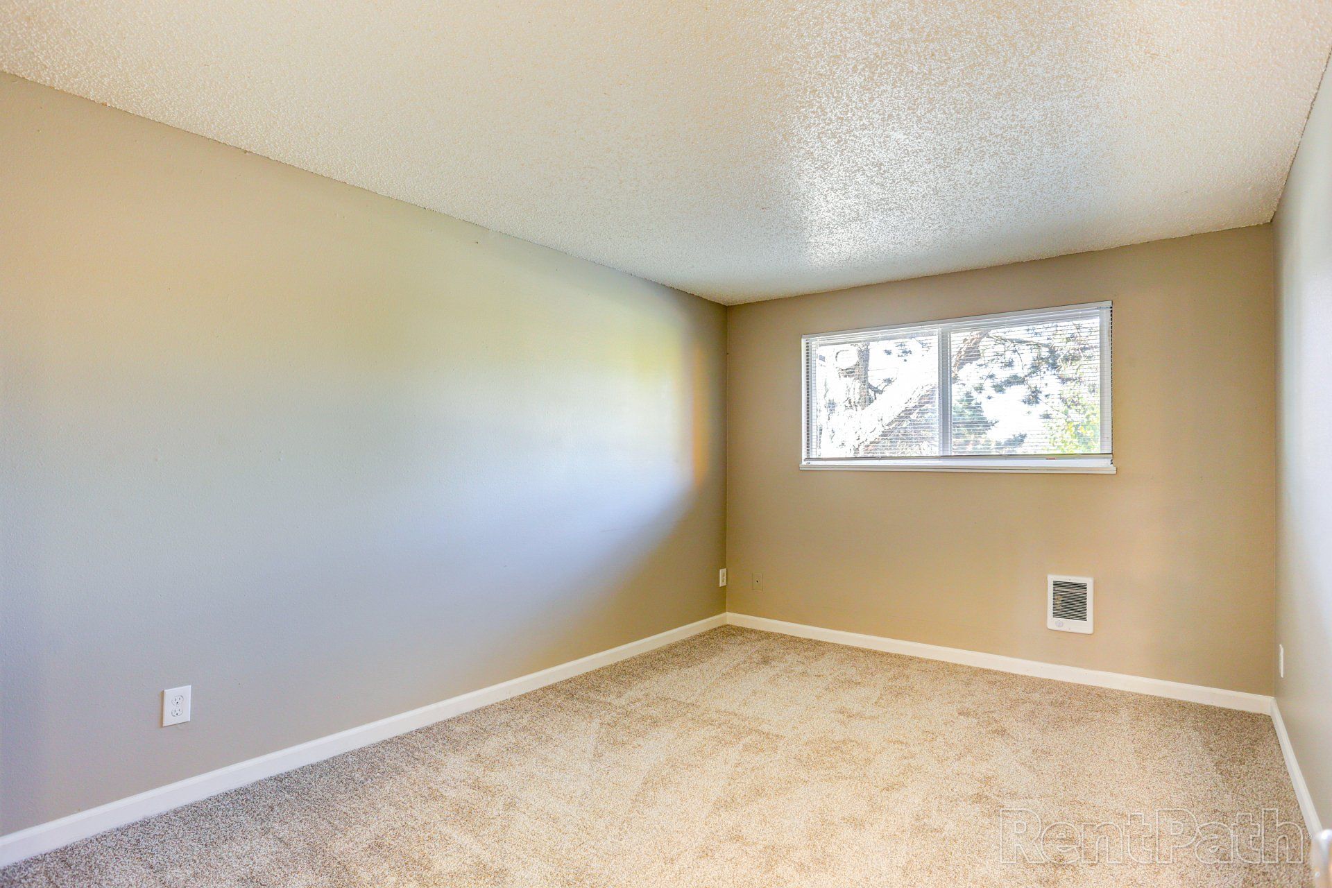 An empty bedroom with a window and carpeted floor.