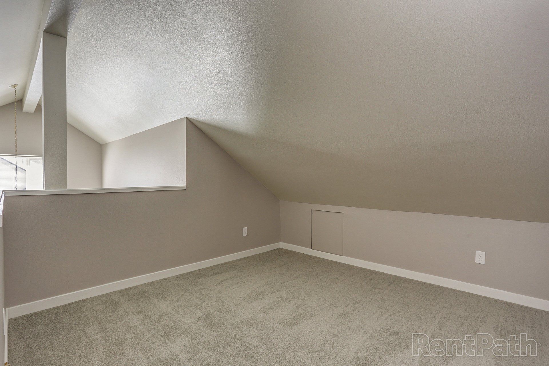 An empty room with a slanted ceiling and a carpeted floor.