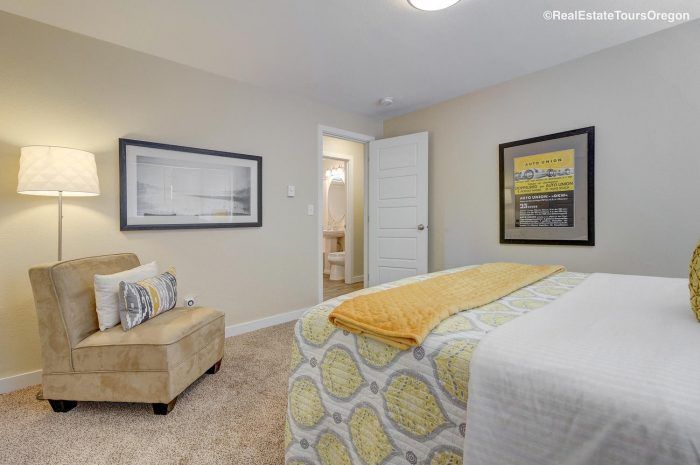 A bedroom with a bed , chair , lamp and paintings on the wall.