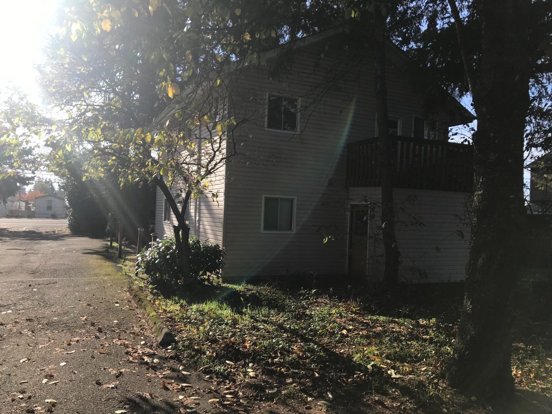 A house with a garage and a balcony is surrounded by trees and leaves.