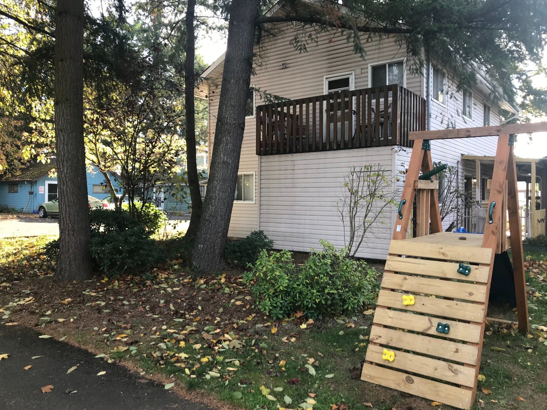 A house with a swing set and a climbing wall in front of it.