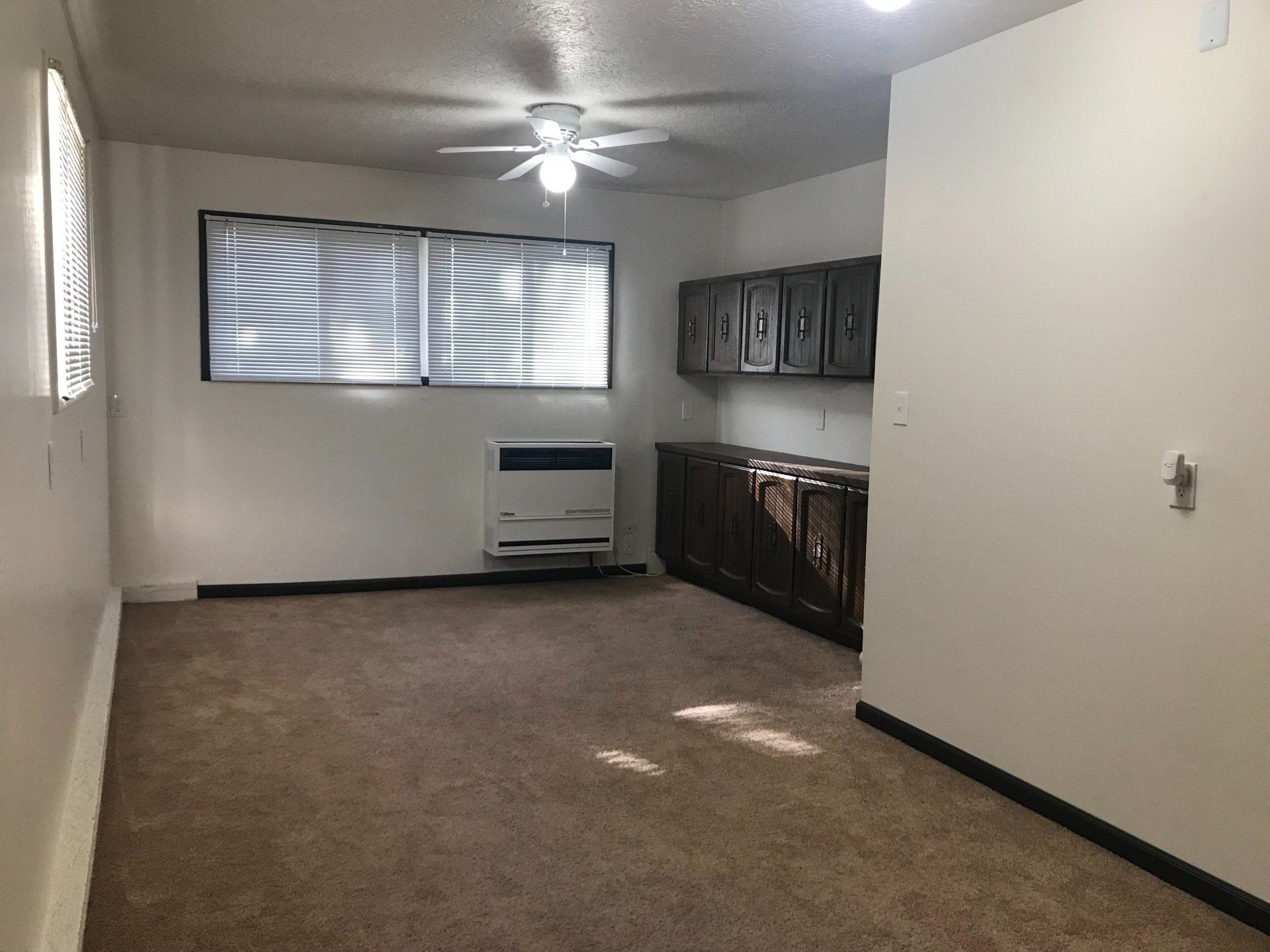 An empty living room with a ceiling fan and a window.