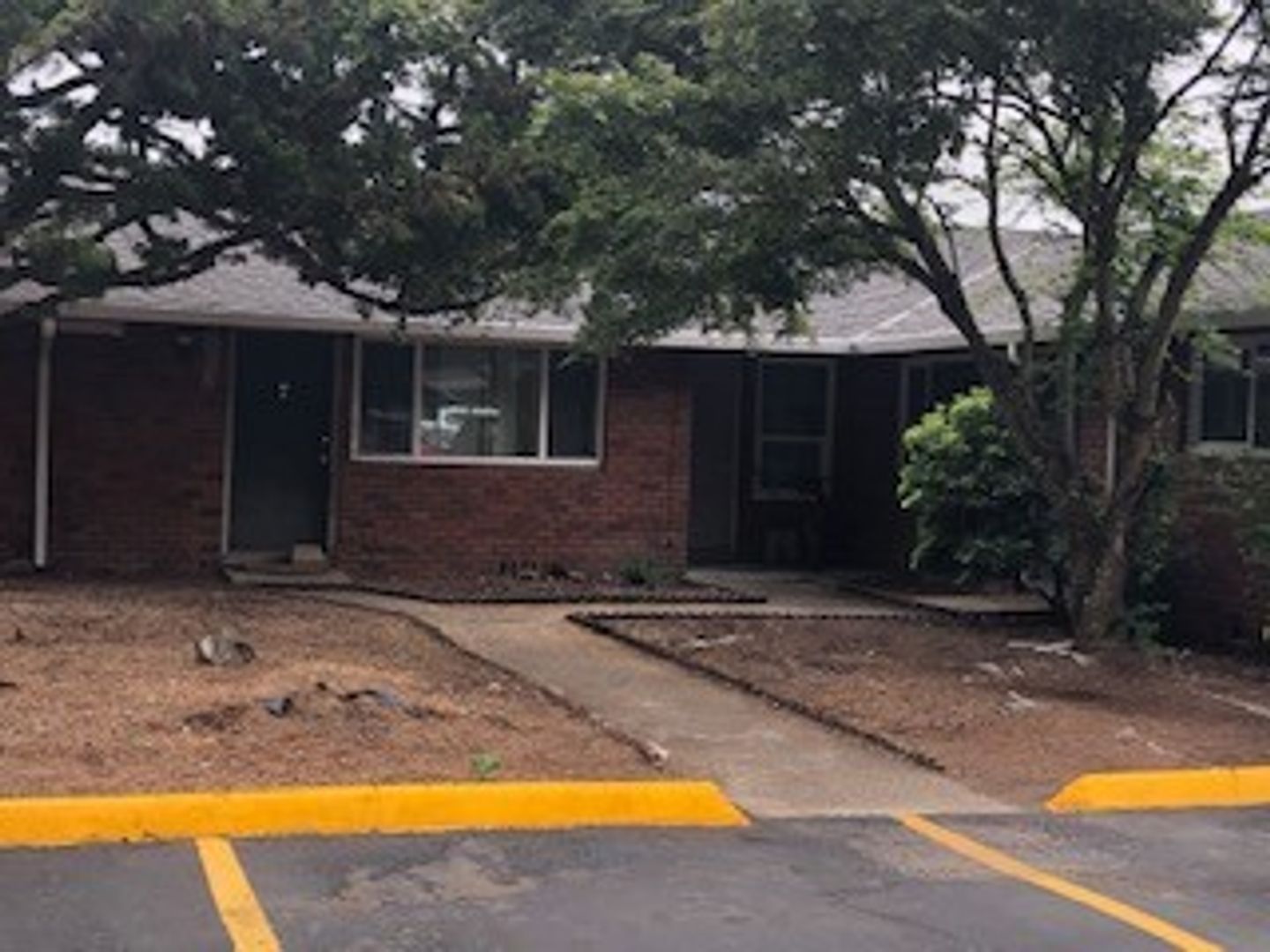 A brick house with a yellow curb and a parking lot in front of it.