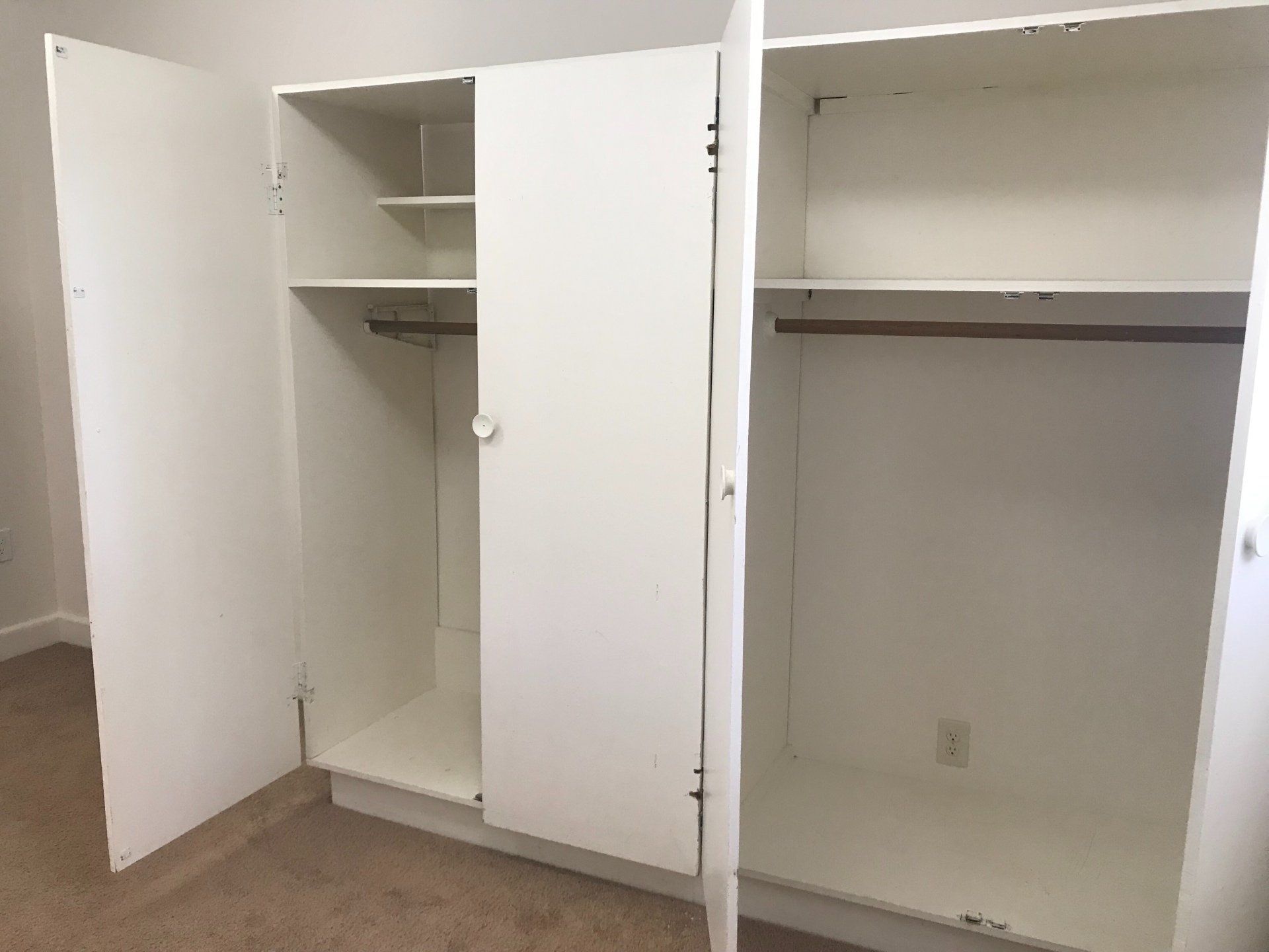 An empty white wardrobe with the doors open in a bedroom.