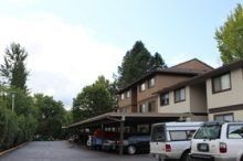 A row of cars are parked under a carport in front of a building.