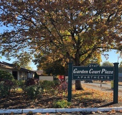 A sign for garden court plaza apartments is in front of a tree