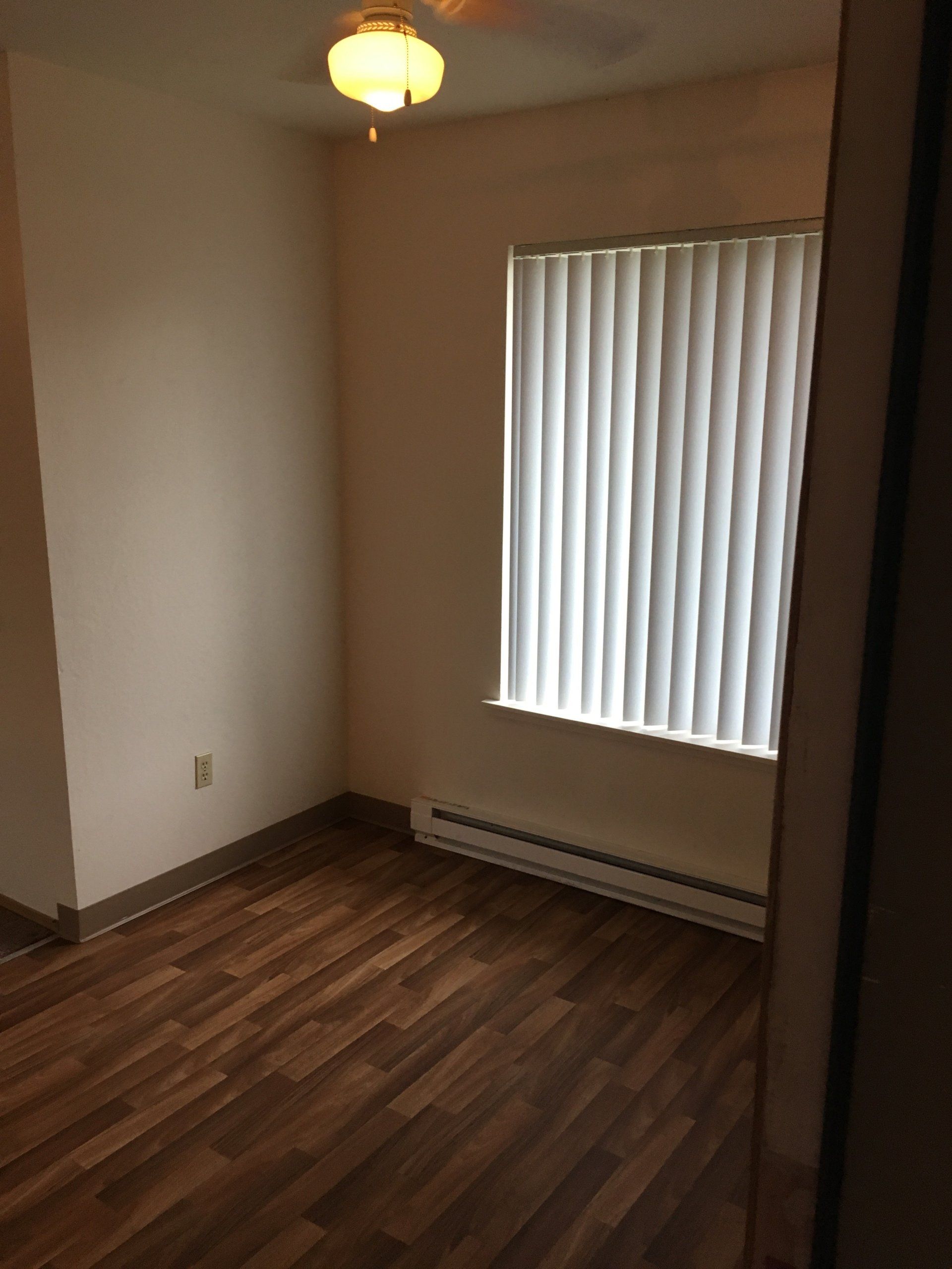 An empty room with hardwood floors and a window with blinds.