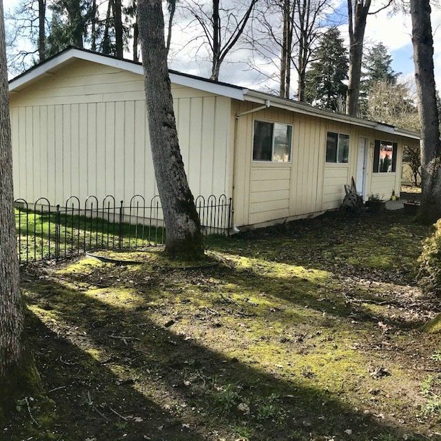 A small house is surrounded by trees and a fence