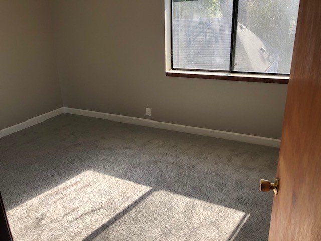 An empty bedroom with a window and a carpeted floor.