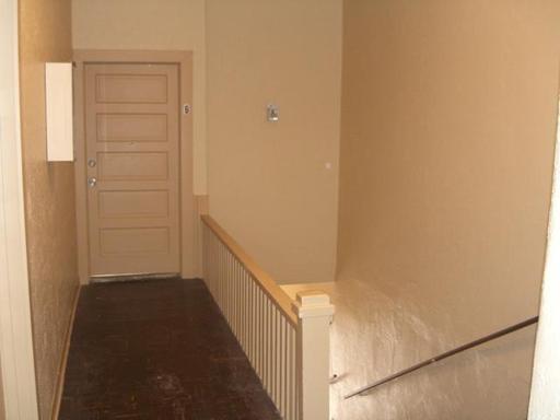 A hallway with stairs leading up to a door and a railing.