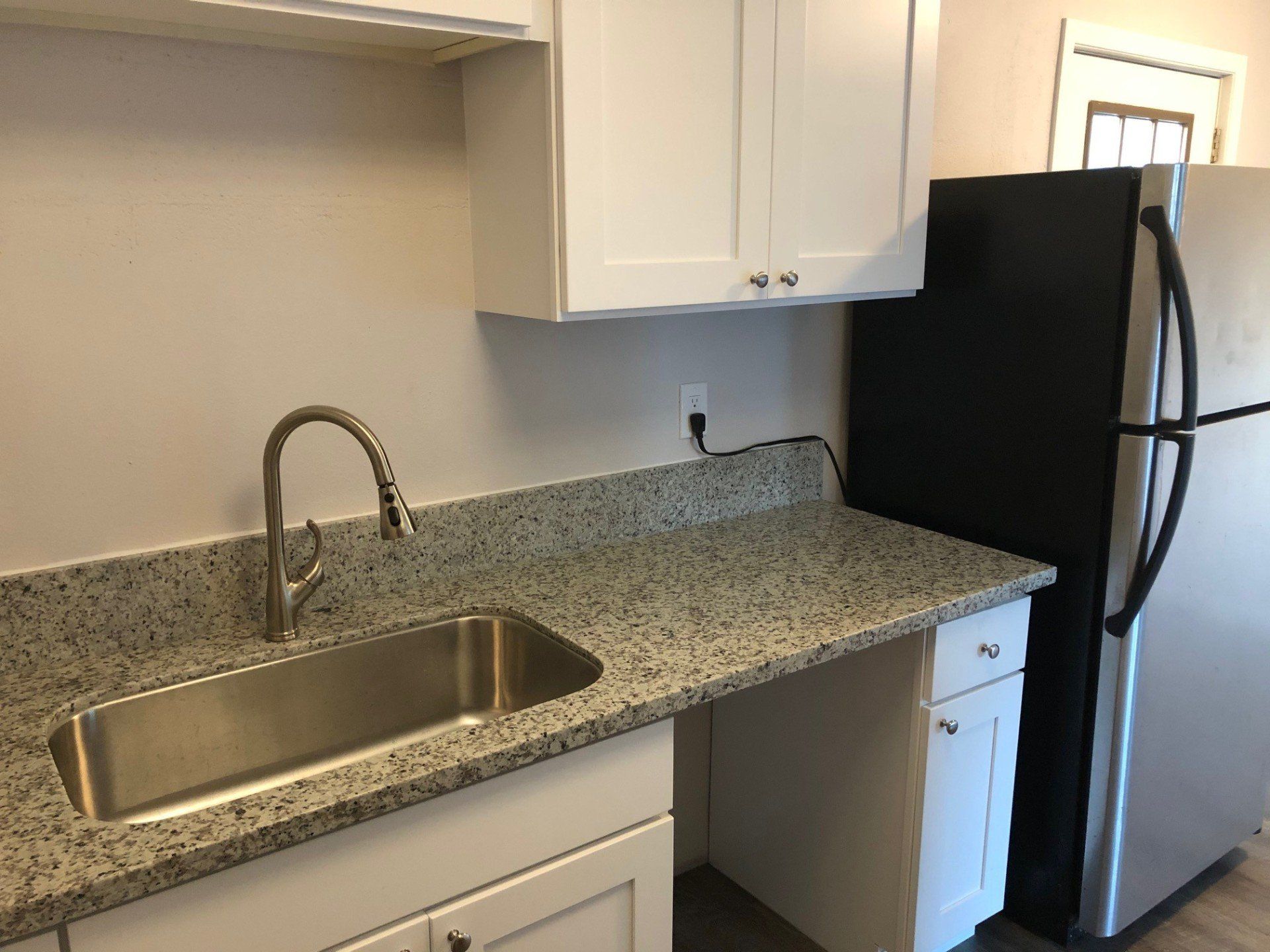 A kitchen with a stainless steel sink and a black refrigerator