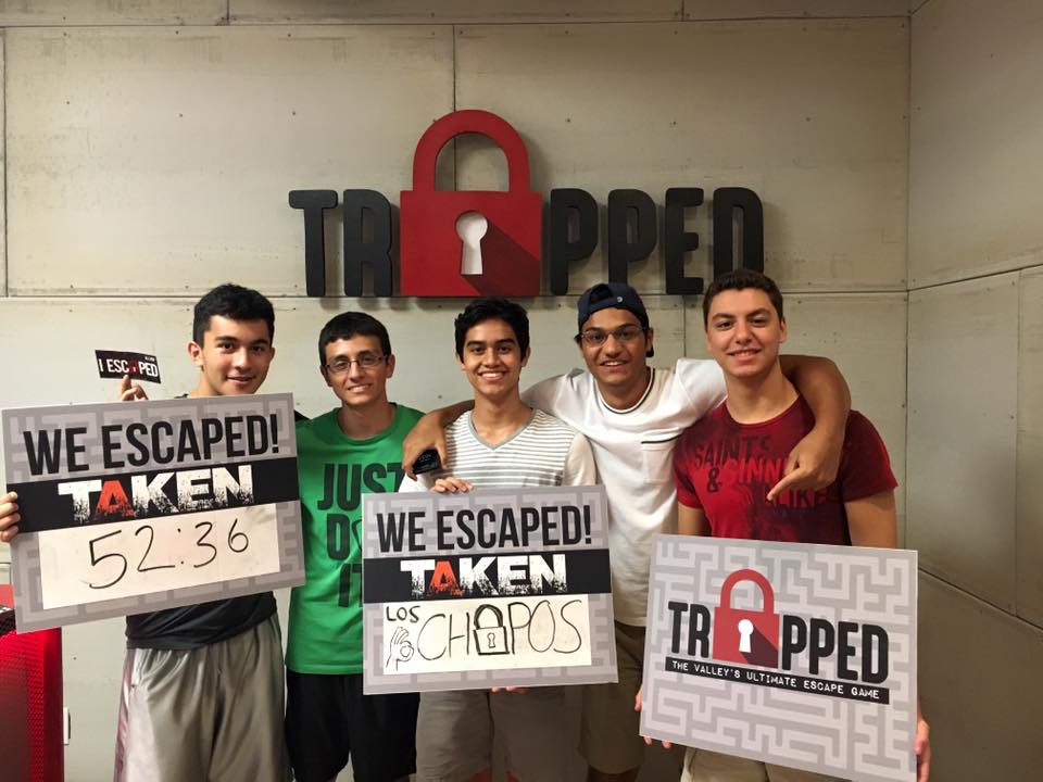 A group of young men are holding signs in front of a wall that says trapped.