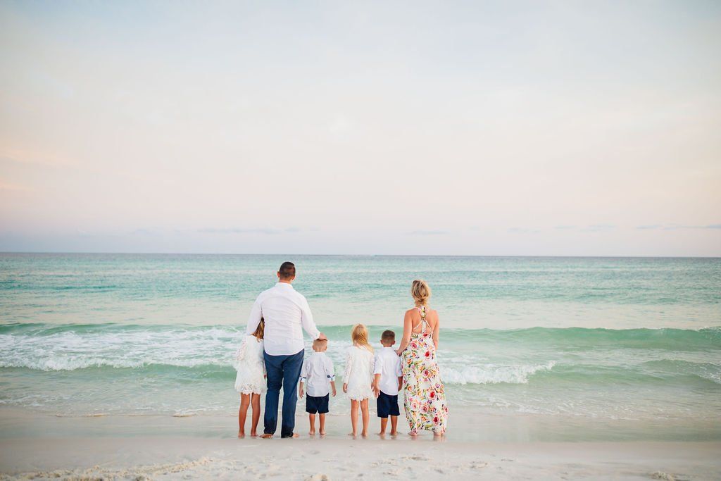family of six looking at the ocean from the beach side shore