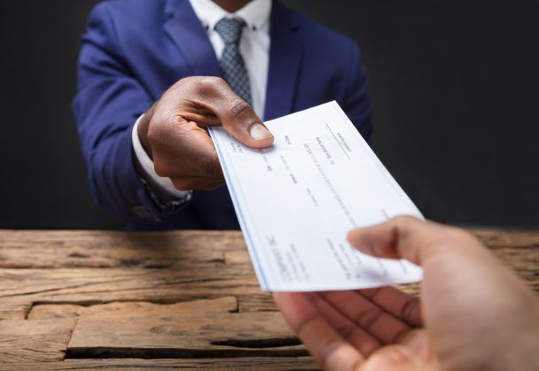 Person in a blue suit handing a check across a wooden table