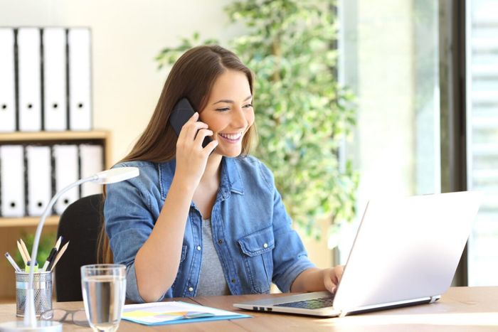 Smiling woman on the phone at a desk with a laptop in a bright office