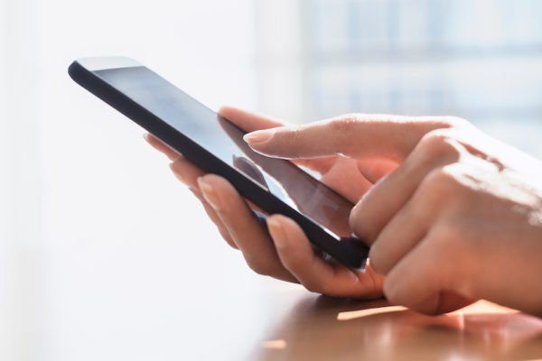 Hands holding a smartphone and tapping the screen on a bright table