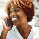 Smiling person with curly hair talking on a cellphone outdoors