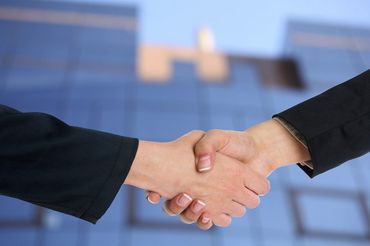 Two people shaking hands in front of a glass office building