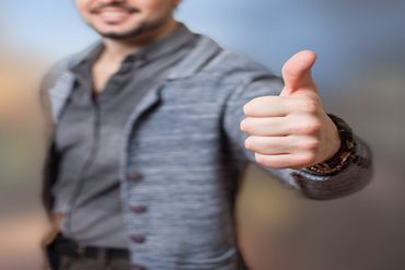 A person in a gray jacket gives a thumbs-up with a blurred background.