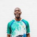 Smiling man in a teal and white sports jersey standing against a white wall