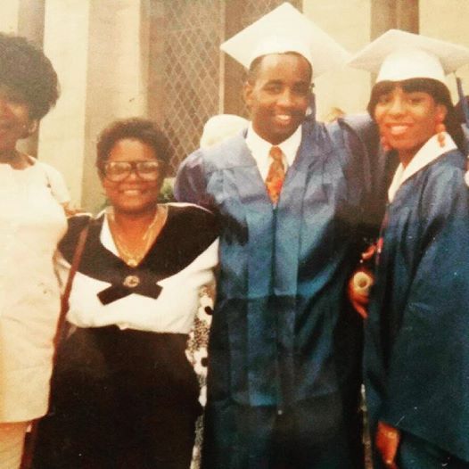 Four people in graduation caps and gowns posing indoors, smiling at the camera.