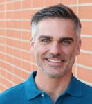 Smiling man in a blue polo shirt standing against a brick wall