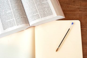 Open book and blank notebook with a pencil on a wooden desk