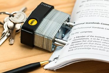 Keys beside a silver padlock securing an open book on a wooden desk