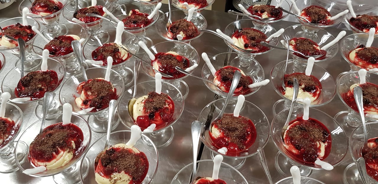 A bunch of desserts in glasses with spoons on a table.