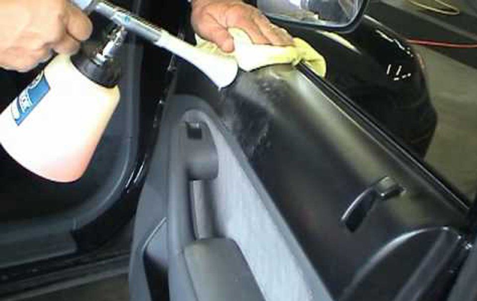 A person is cleaning a car door with a spray bottle.
