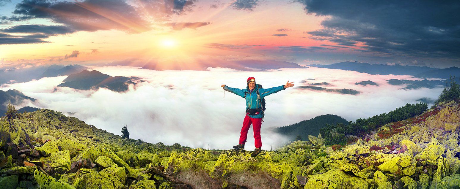 Hiker on a ridge with arms outstretched in front of a glorious sunset.
