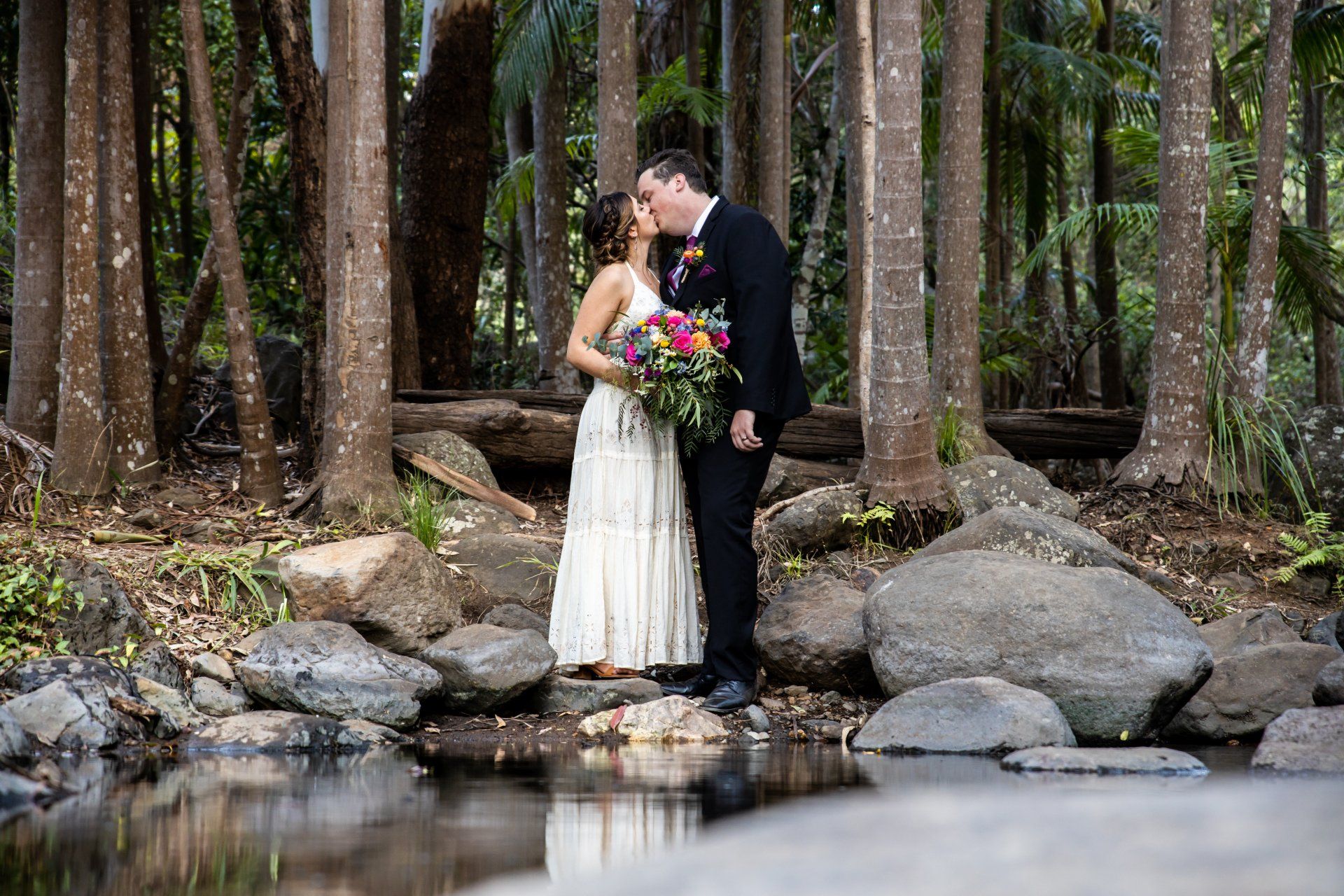 a bride and groom are kissing in the woods near a river .