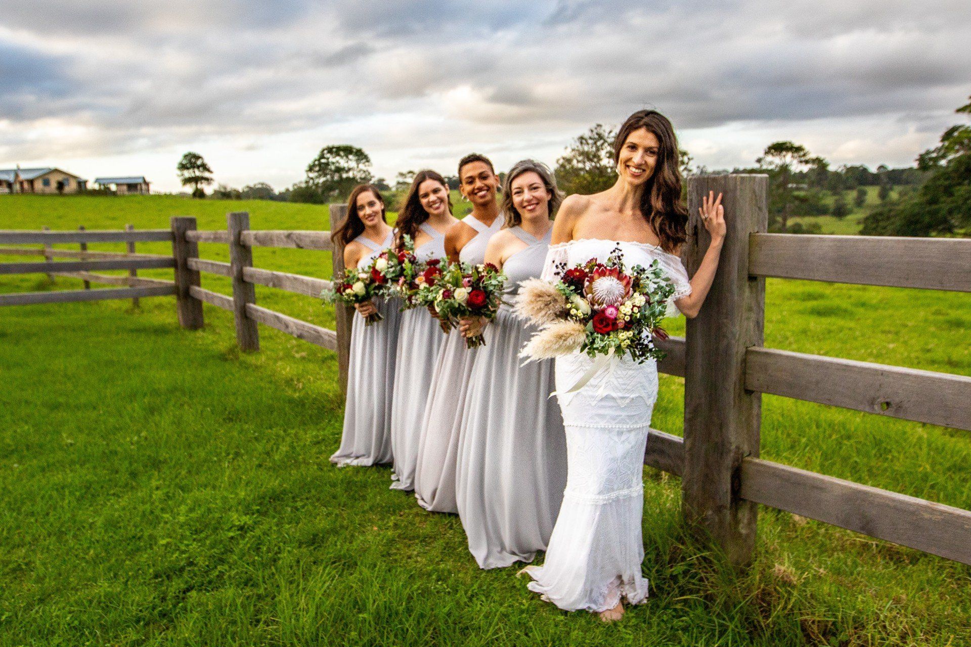 a bride and her bridesmaids are standing next to a wooden fence in a field .