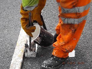 For road marking application in Colchester call Eastern Road Markings Man pouring paint into line marker on the road