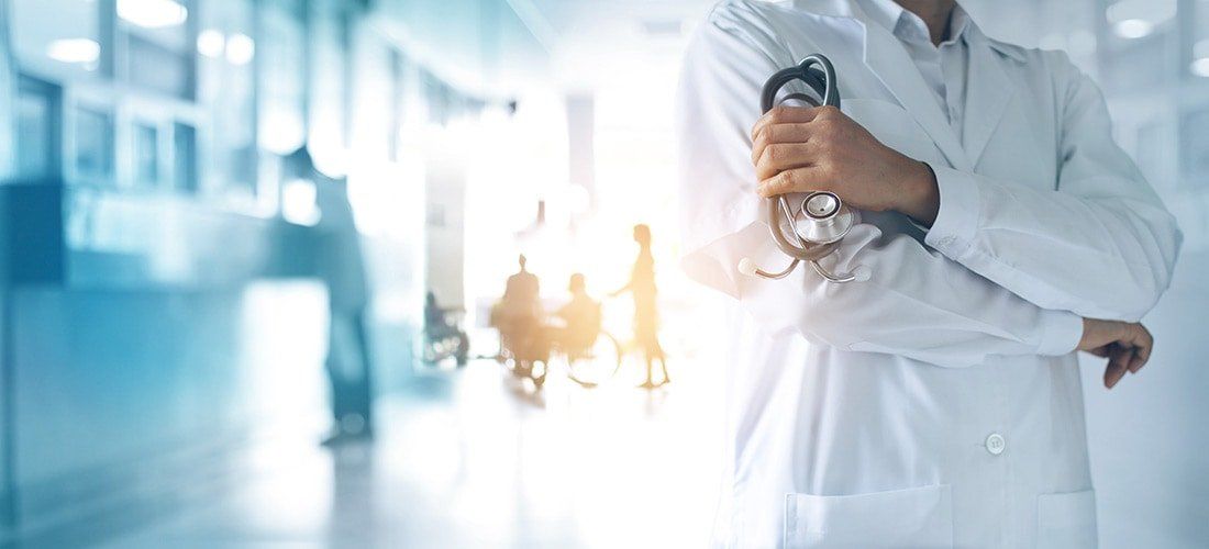 A doctor is holding a stethoscope in a hospital hallway.