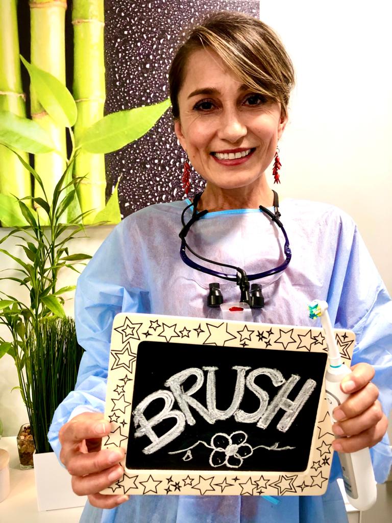 Woman in apron holding a blackboard sign that says “BRUSH,” with bamboo plants in the background.