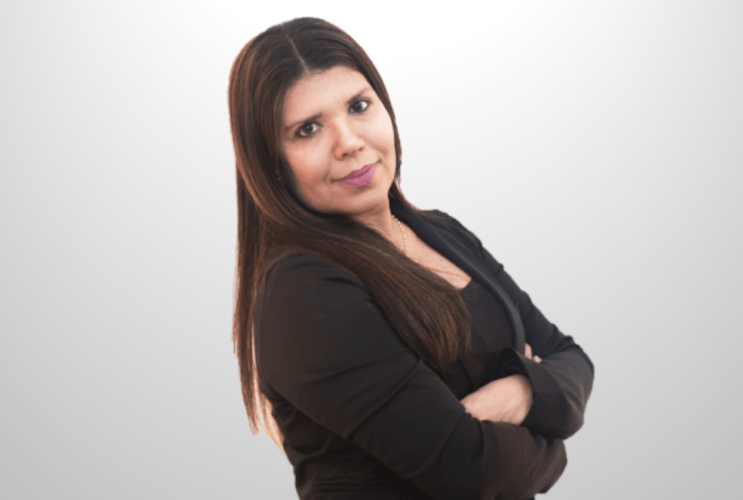 Mulher sorridente com longos cabelos castanhos, braços cruzados, vestindo uma blusa preta contra um fundo branco.