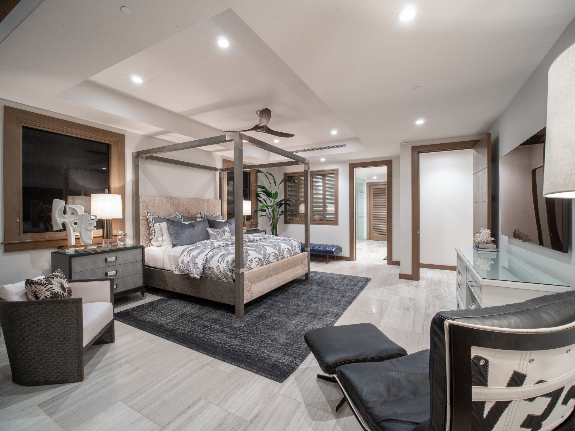 A bedroom with a canopy bed , chair , ottoman and television.