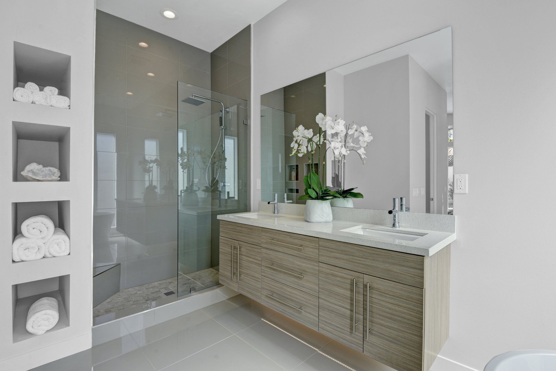 A bathroom with two sinks , a large mirror and a walk in shower.