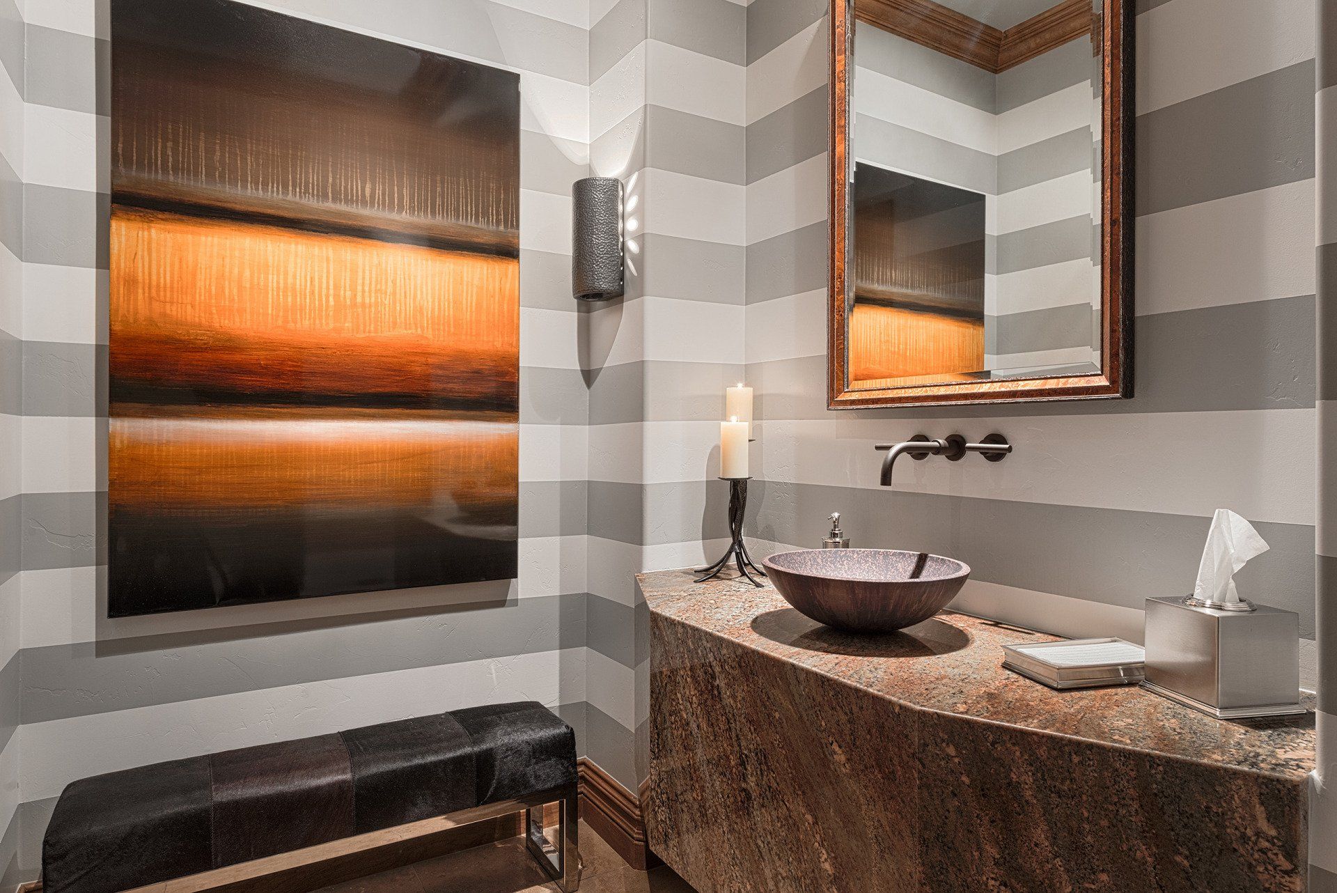 A bathroom with striped walls , a sink , a mirror and a bench.