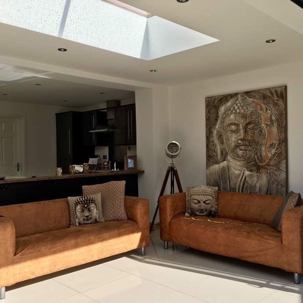 Two brown leather sofas in a modern living room, featuring Buddha-themed cushions and artwork, with a skylight above.