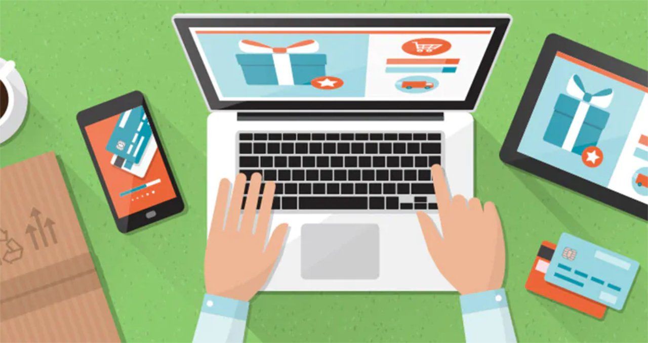 A person is typing on a laptop computer surrounded by a tablet , phone , and credit card.