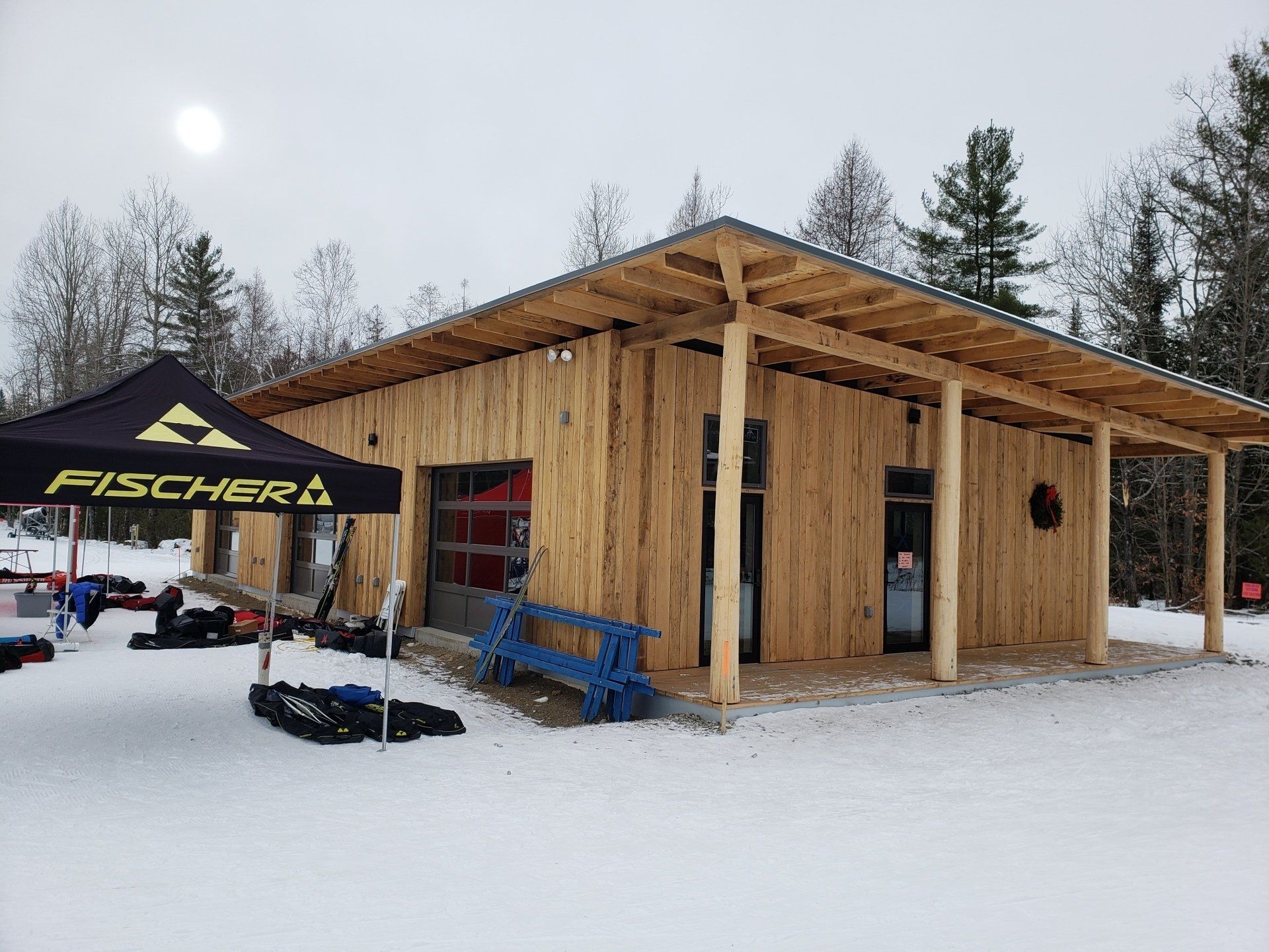 Small wooden ski hut with a black Fischer tent and snow-covered ground in a winter forest.