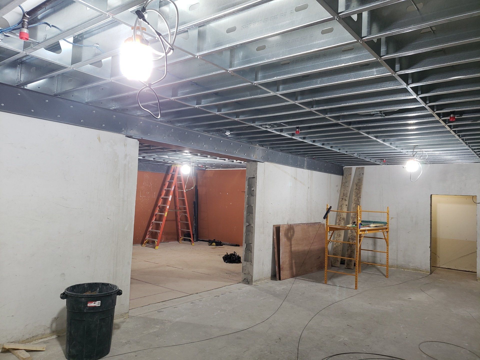 Construction site with exposed ceiling grid, ladders, tools, and unfinished walls in a large room