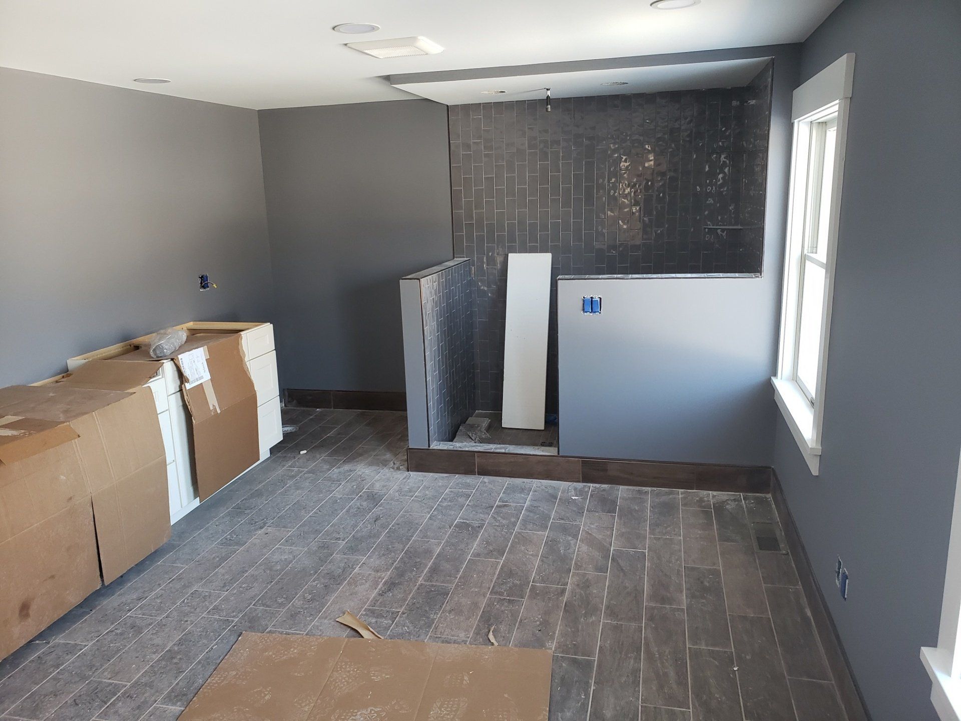 Empty room under renovation with gray walls, cardboard boxes, and unfinished floor.