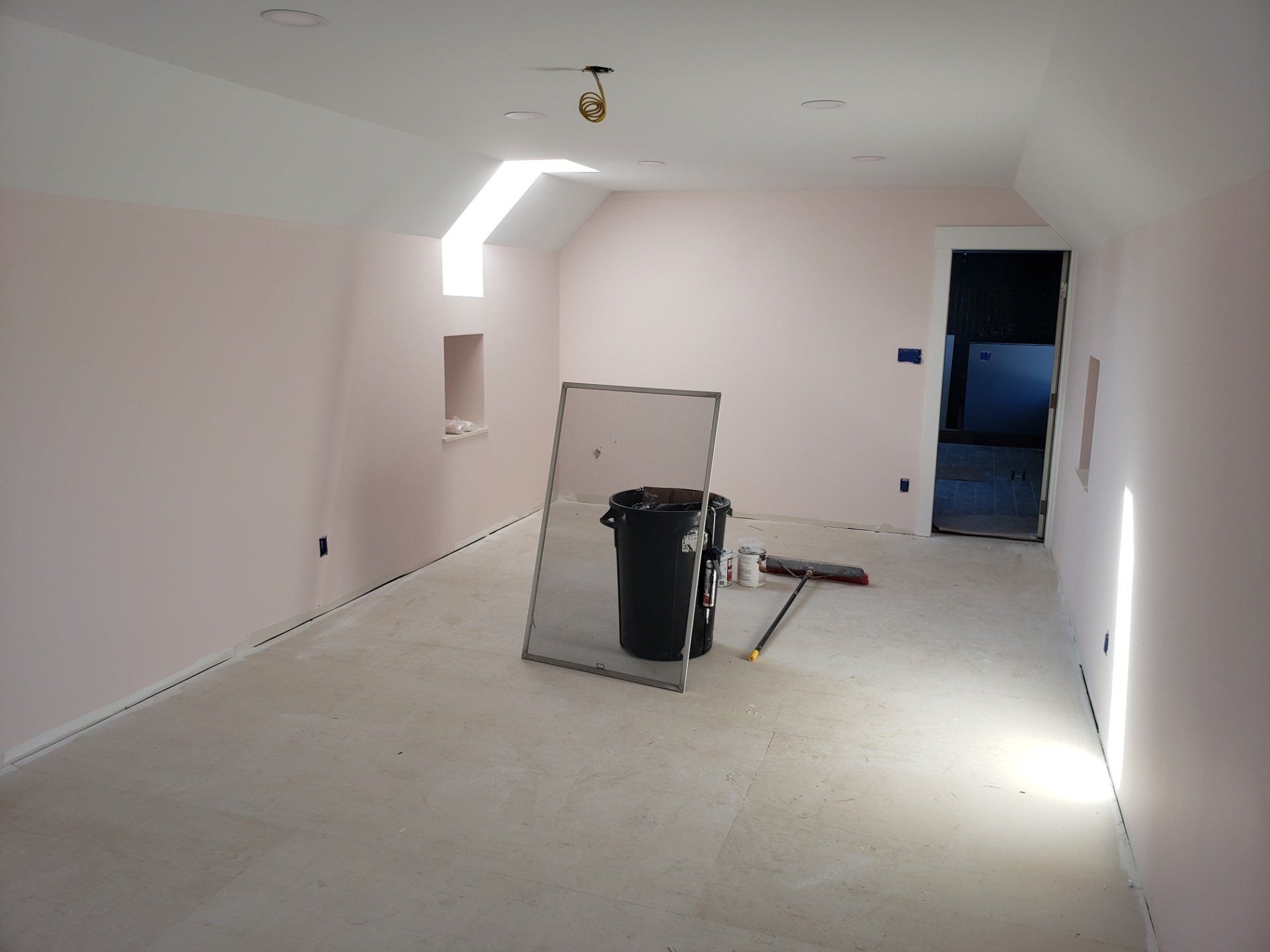 Empty white room under renovation with drywall tools, a ladder, and bright light from the ceiling.