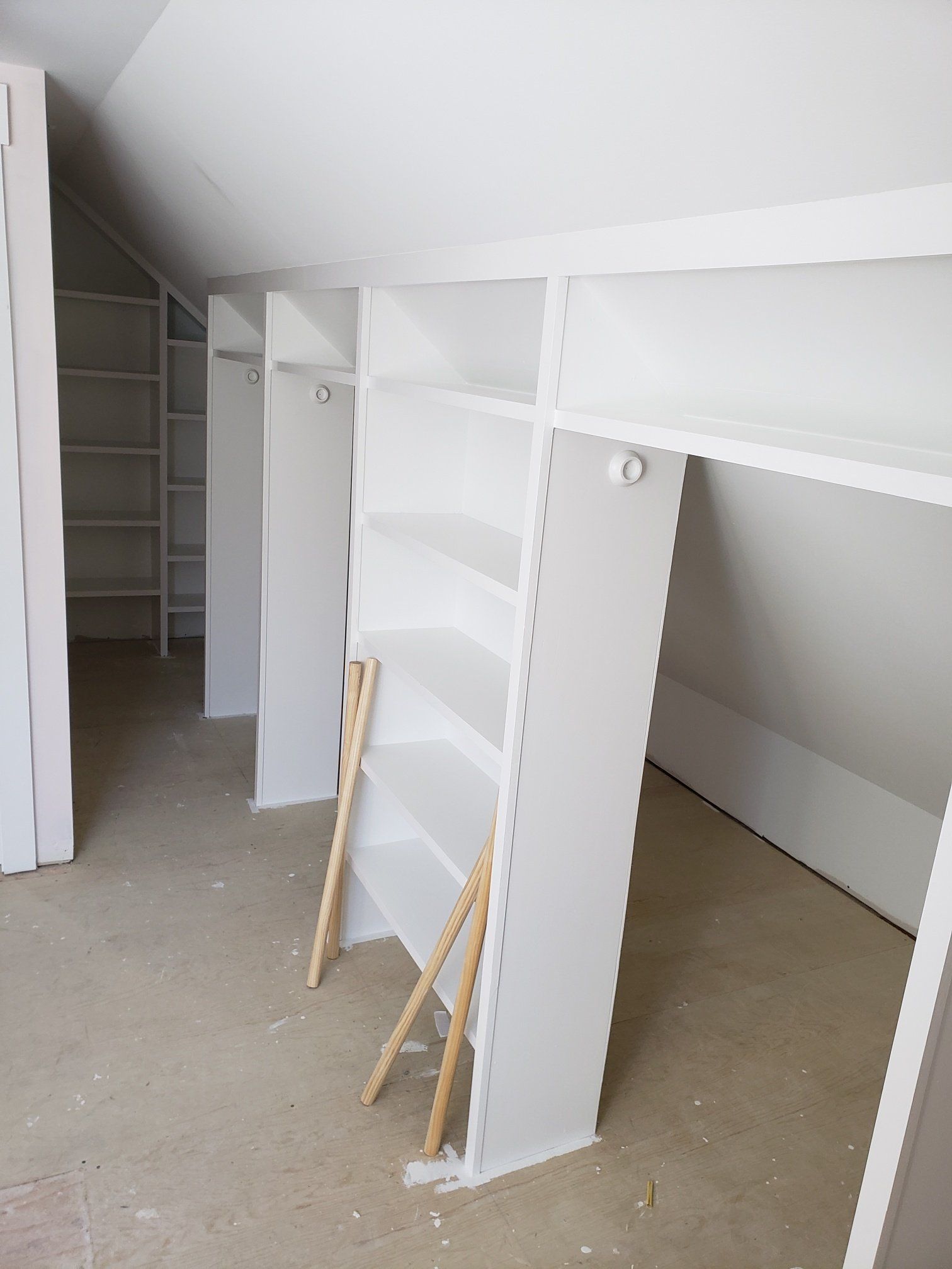 Unfinished white built-in shelving and closet units in a bare room under construction.